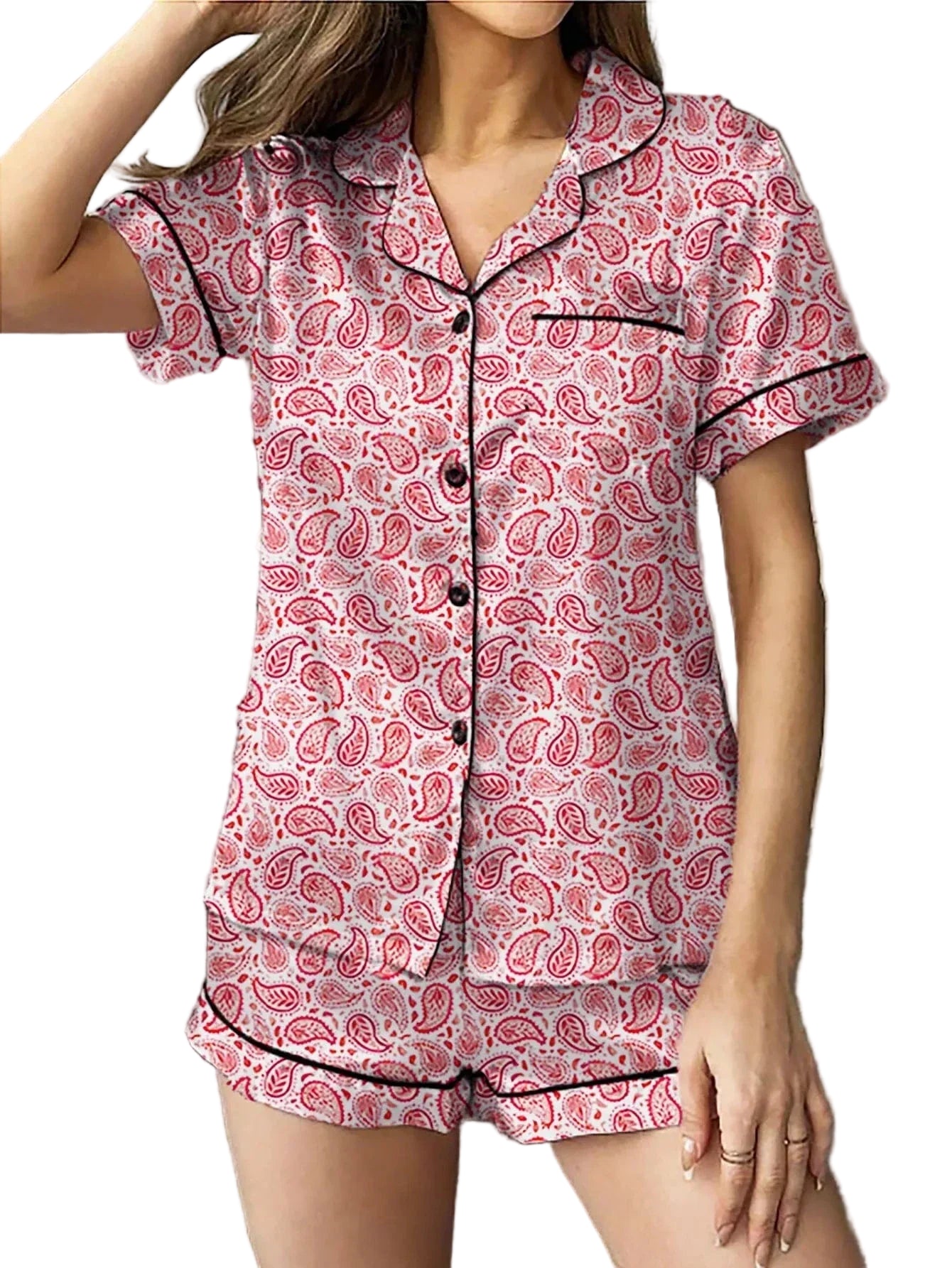 Femme portant un pyjama deux pièces à motifs cachemire rouges et roses sur fond clair, composé d’un haut boutonné à manches courtes avec col et passepoils noirs, et d’un short assorti. Ensemble fluide, léger et confortable, idéal pour l’été ou les nuits paisibles à la maison.