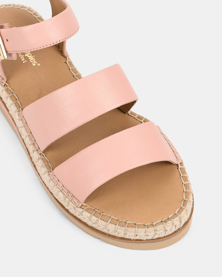 Gros plan sur les lanières en cuir rose clair des sandales, avec une semelle en jute tressé qui ajoute une touche d&