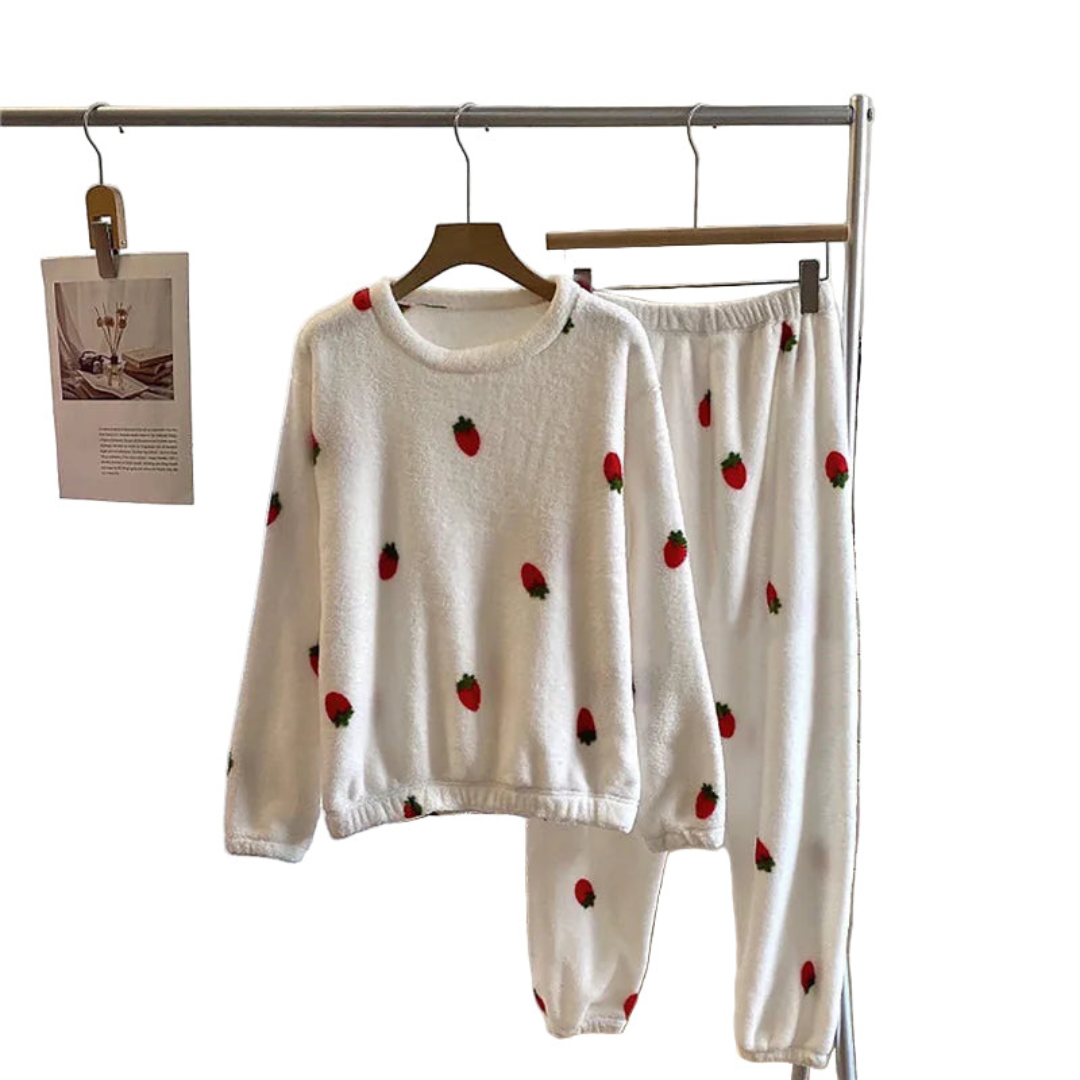Pyjama femme en peluche blanche avec des motifs de fraises rouges, comprenant un sweat à manches longues avec un col rond et un pantalon assorti avec une taille élastique, suspendus sur un porte-vêtements, pour un look cosy et amusant.