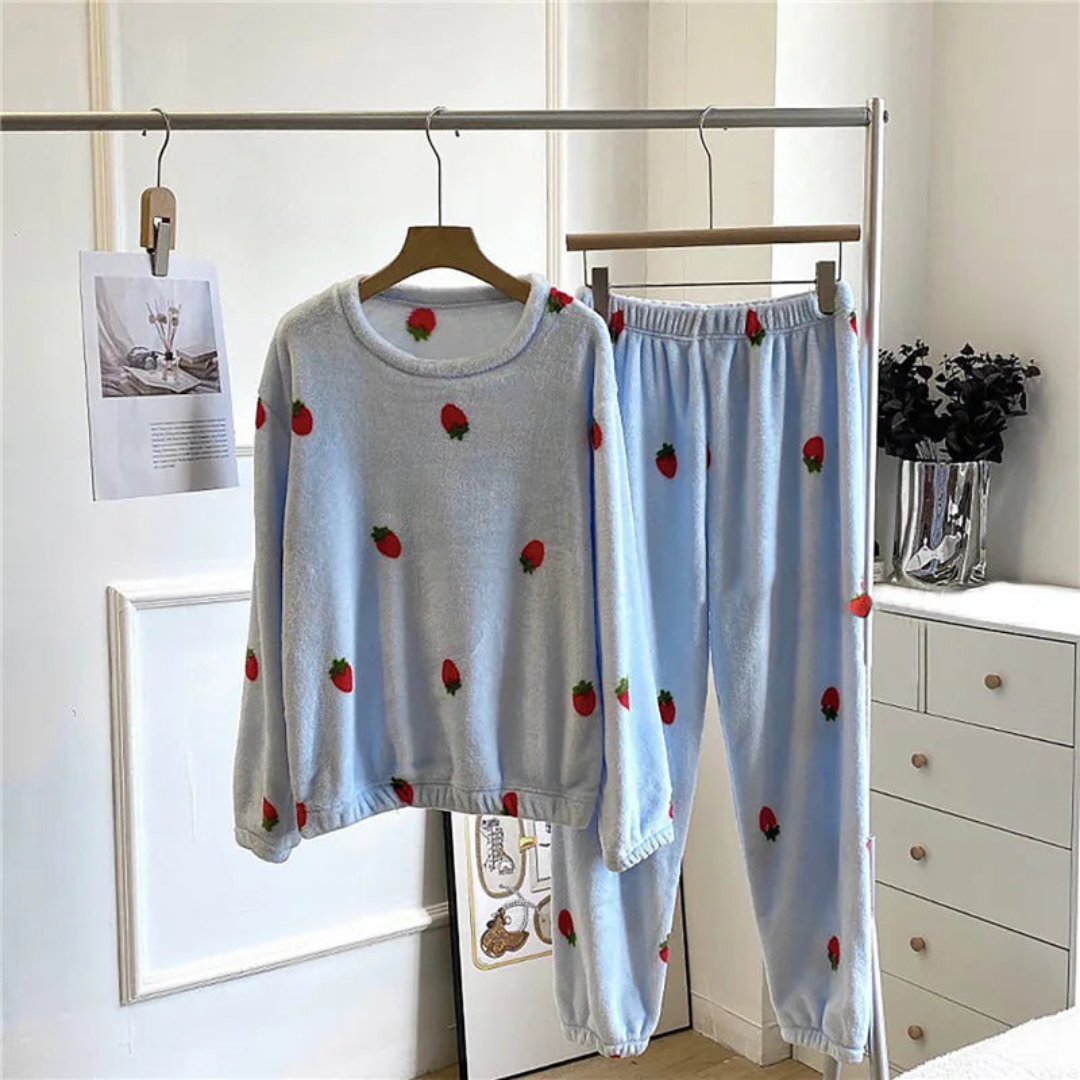 Pyjama femme en peluche bleue avec des motifs de fraises rouges, comprenant un sweat à manches longues avec un col rond et un pantalon assorti avec une taille élastique, suspendus sur un porte-vêtements, pour un look cosy et fruité.
