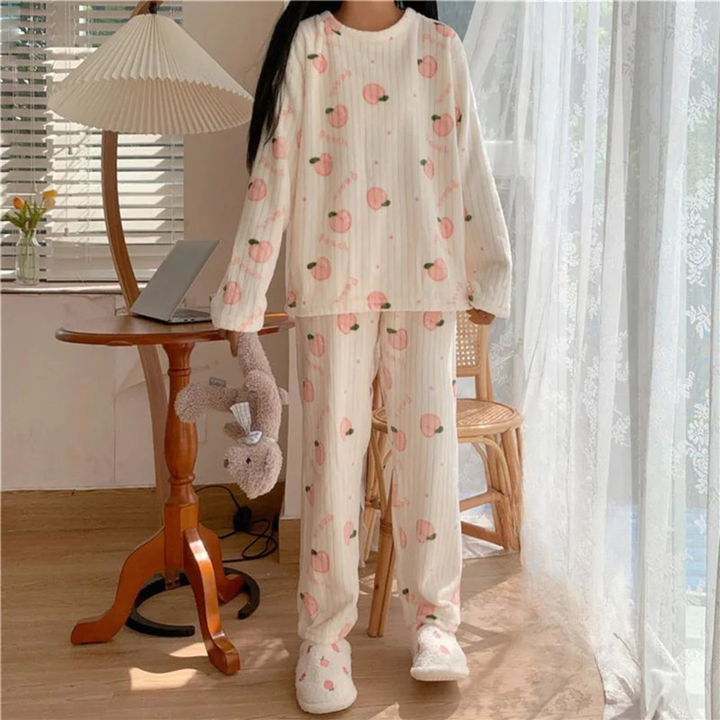 Pyjama femme en peluche douce de couleur blanche avec des motifs de pêches roses. La personne porte le pyjama et se tient debout près d&