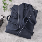 Peignoir Michel pour homme, modèle doux et agréable en tissu texturé bleu marine avec liseré blanc, présenté plié sur une surface en pierre avec accessoires de salle de bain.