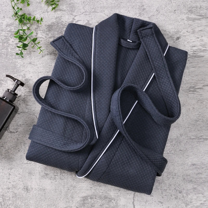 Peignoir Michel pour homme, modèle doux et agréable en tissu texturé bleu marine avec liseré blanc, présenté plié sur une surface en pierre avec accessoires de salle de bain.