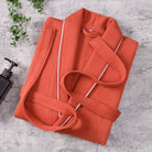 Peignoir Michel pour homme, modèle doux et agréable en tissu texturé orange avec liseré blanc, présenté plié sur une surface en pierre avec accessoires de salle de bain.