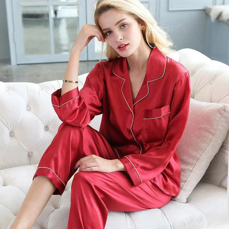 Femme portant le pyjama Mirella en satin rouge avec des détails blancs, un ensemble doux et confortable, assise sur un canapé et affichant un regard détendu et élégant.