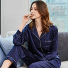 Femme portant le pyjama satin Mirella bleu nuit, avec des détails blancs, assise sur un canapé et affichant un regard détendu et élégant, mettant en valeur le confort et la douceur du pyjama.