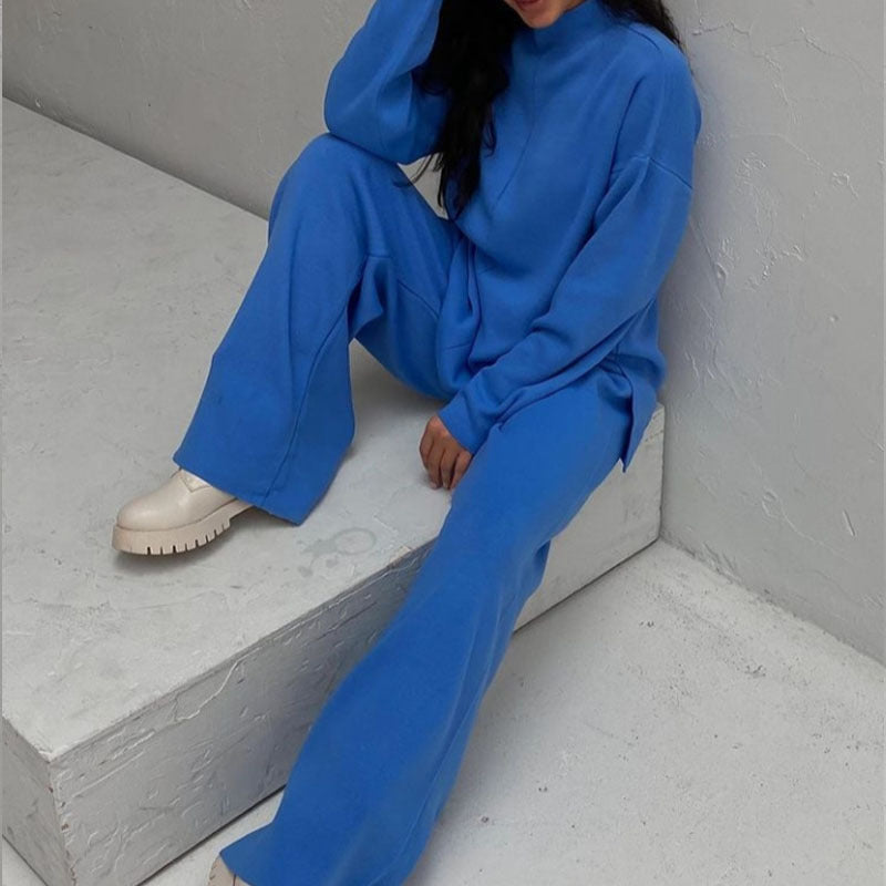 Femme assise portant l’ensemble Naïla bleu cobalt, composé d’un pull oversize à col montant et manches longues, assorti à un pantalon large confortable. Tenue douce et chaude, idéale pour un look cozy et tendance pendant les journées fraîches.