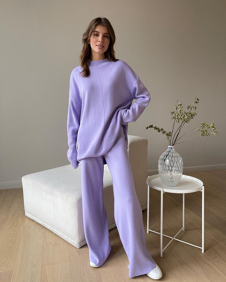 Femme portant l’ensemble Naïla en maille lavande, composé d’un pull oversize à col montant et manches longues, et d’un pantalon large assorti. Tenue douce, chaude et élégante, parfaite pour un look cocooning tendance à la maison ou en intérieur chic.