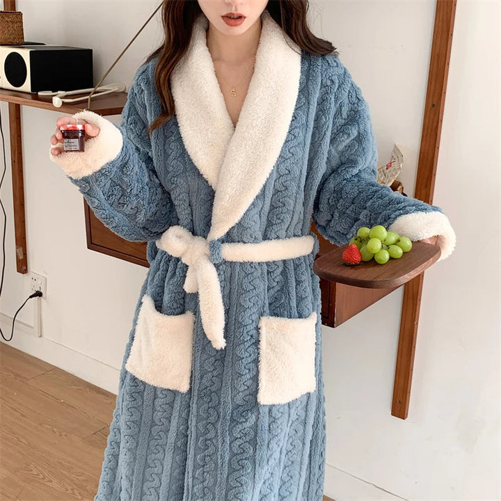 Peignoir femme chaud et confortable Nancy en tissu peluche bleu à motif torsadé, col châle blanc, ceinture et grandes poches contrastées, porté en intérieur.