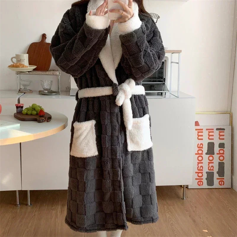 Peignoir femme chaud et confortable  Nancy  en tissu peluche gris anthracite à effet matelassé, col châle blanc, ceinture et poches contrastées, porté en intérieur.