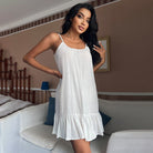 modèle en nuisette blanche fluide à fines bretelles, coupe ample avec volant en bas, portée en intérieur.