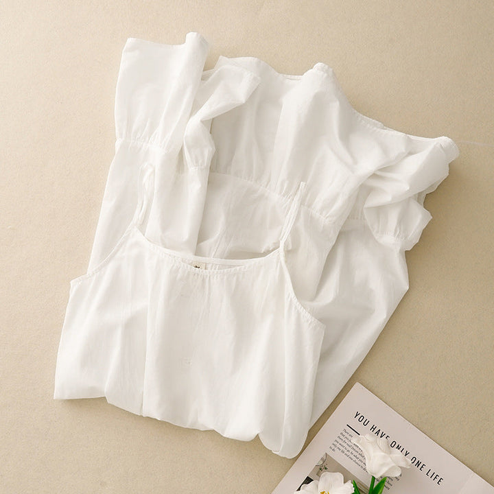  ensemble de nuit blanc plié, comprenant une nuisette à fines bretelles et un peignoir léger, posé sur un fond beige.