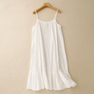 nuisette blanche fluide à fines bretelles, coupe ample avec volant au bas, suspendue sur cintre devant un mur beige.