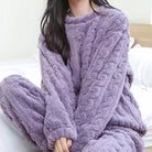 Femme assise sur un lit, habillée d’un pyjama polaire violet avec effet torsadé, comprenant un haut à manches longues et un pantalon assorti. Ensemble douillet, chaud et ultra confortable, parfait pour les journées cocooning ou les soirées d’hiver à la maison.