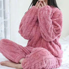 Femme assise sur un lit, portant un pyjama polaire rose à texture torsadée, composé d’un haut manches longues et d’un pantalon assorti. Ensemble chaud, ultra doux et confortable, parfait pour affronter l’hiver avec style et bien-être.