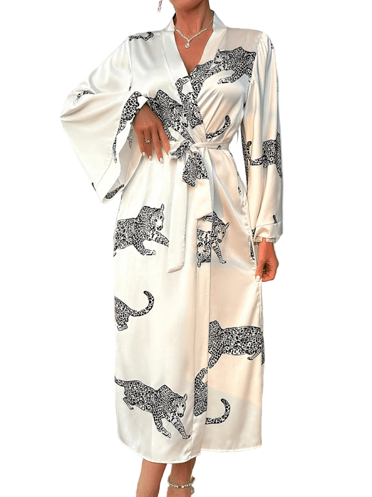 Femme portant le peignoir Noelia en satin blanc avec motifs léopard noirs, coupe longue à manches larges et ceinture à nouer à la taille. Modèle tendance et agréable, idéal pour des instants de détente élégants à la maison.