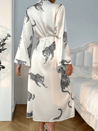 Vue arrière du peignoir Noelia porté par une femme, en satin blanc imprimé léopard noir, avec manches longues évasées et ceinture à nouer à la taille. Peignoir fluide et raffiné, parfait pour une allure élégante et confortable à la maison.