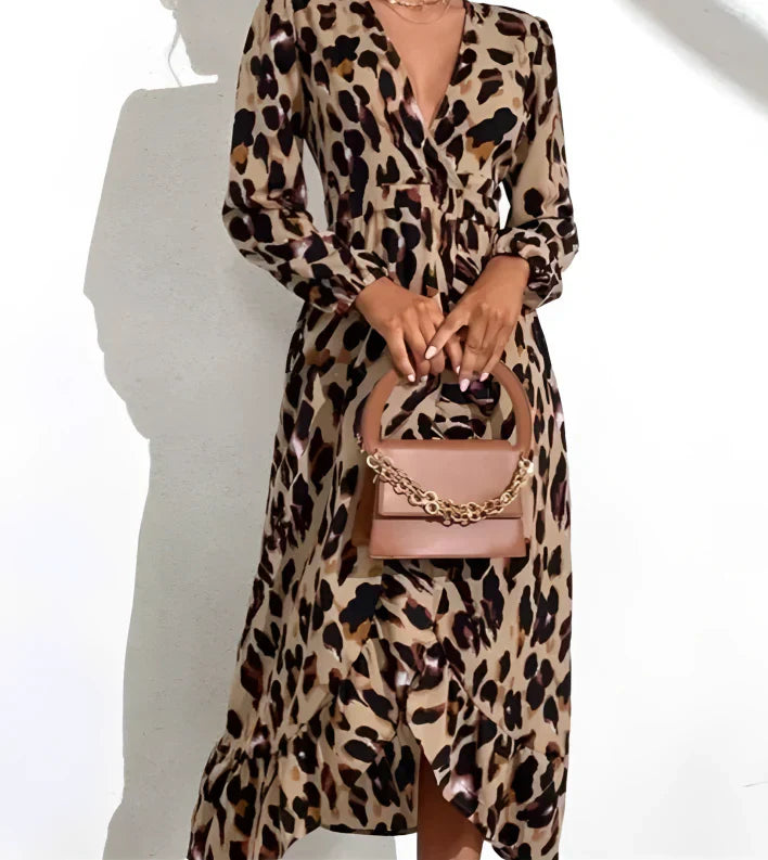Femme portant une robe léopard à manches longues et fente sur le côté, avec un sac à main beige, devant un fond blanc.