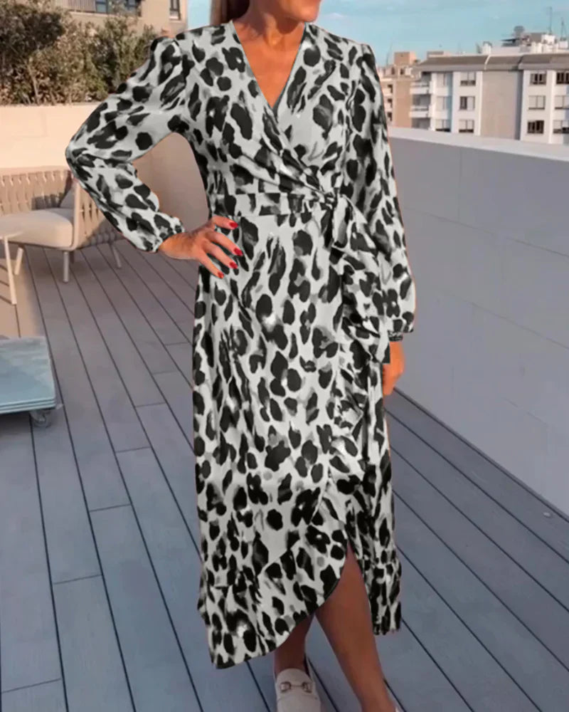 Femme portant une robe longue à imprimé léopard noir et blanc, avec une coupe croisée, une fente sur le côté et un détail de ceinture, créant une silhouette chic et fluide.