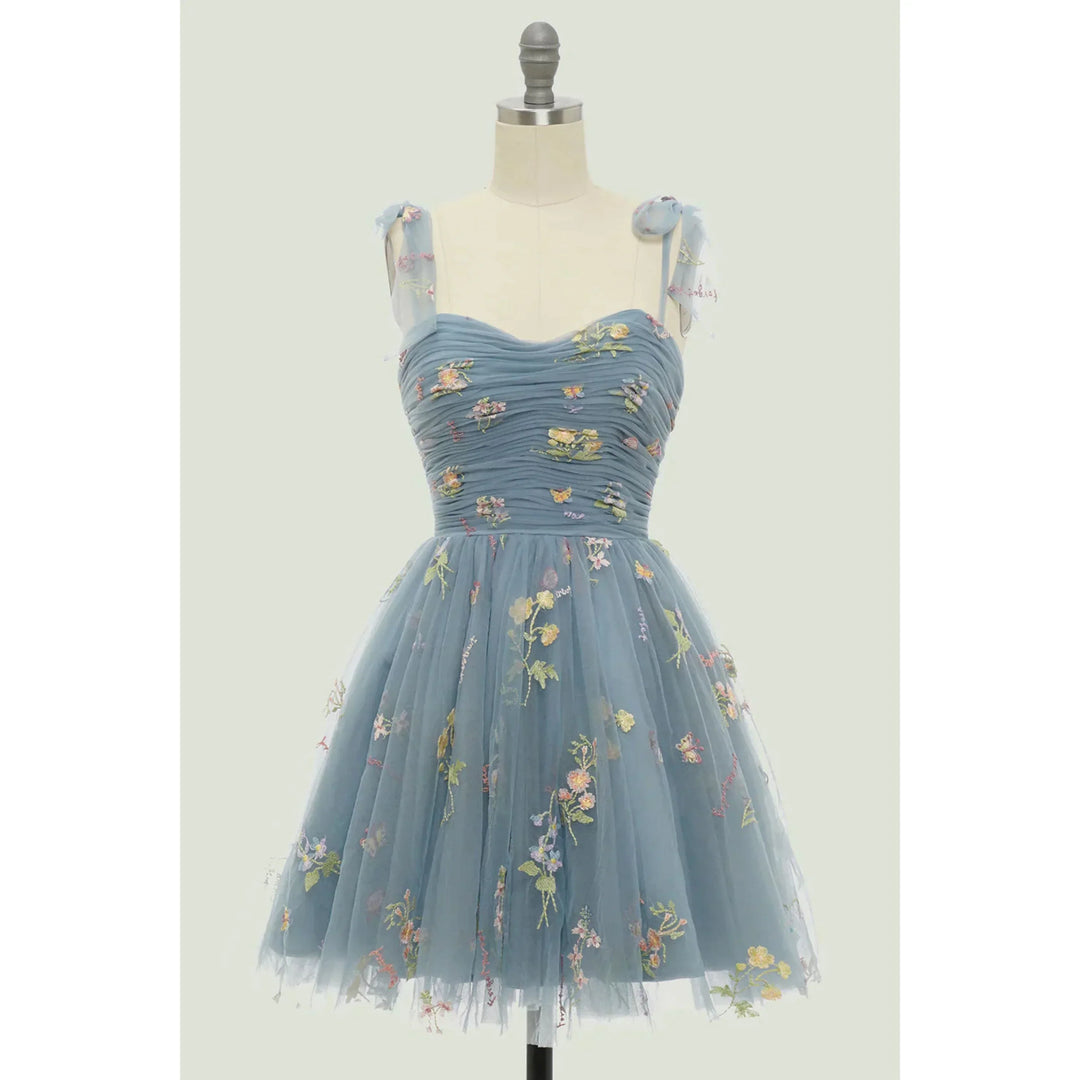 Bleu ciel en tulle brodé de fleurs, bustier plissé, bretelles en voile nouées et taille cintrée, avec jupe courte évasée, présentée sur mannequin.