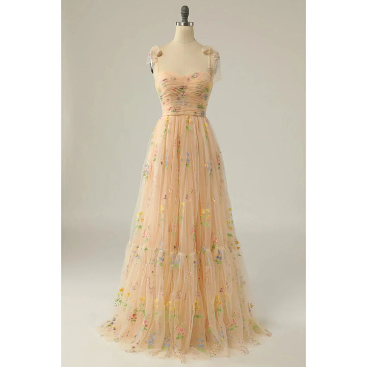 Beige nude en tulle brodé de fleurs multicolores, bustier plissé, fines bretelles en voile et jupe fluide évasée, présentée sur mannequin.