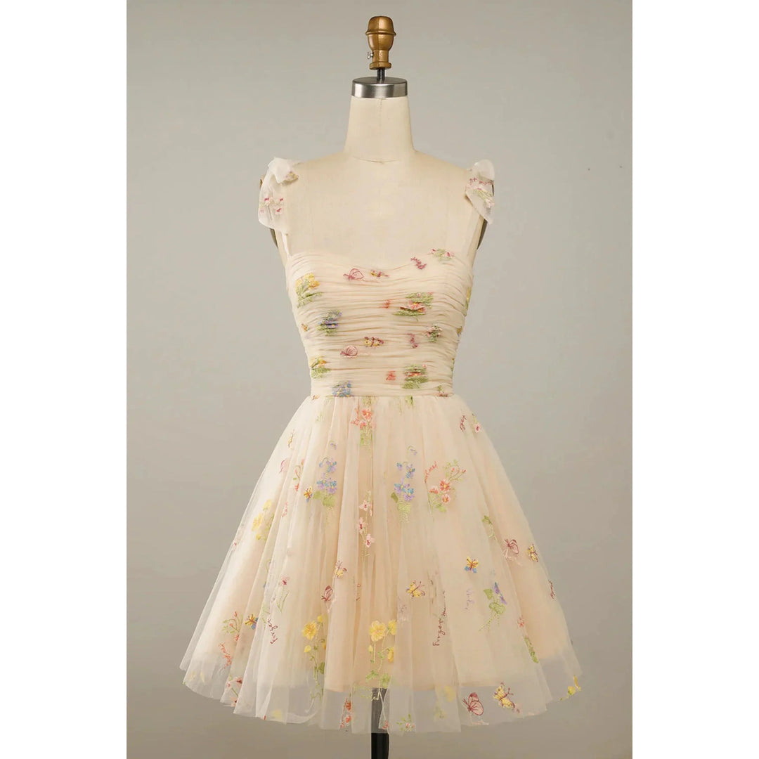 Beige nude en tulle brodé de fleurs multicolores, bustier plissé, petites manches en voile et taille cintrée, avec jupe courte évasée, sur mannequin.