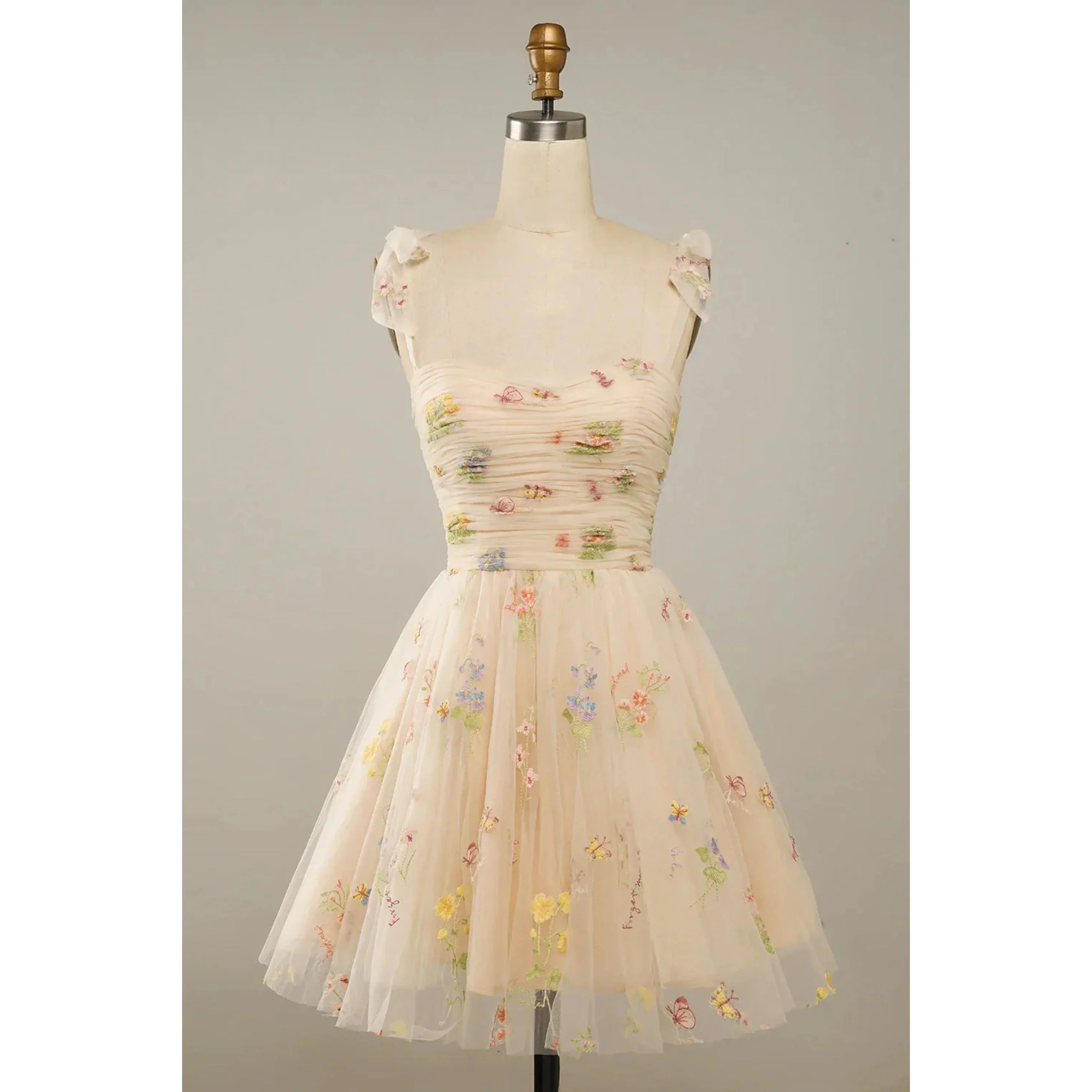 Beige nude en tulle brodé de fleurs multicolores, bustier plissé, petites manches en voile et taille cintrée, avec jupe courte évasée, sur mannequin.