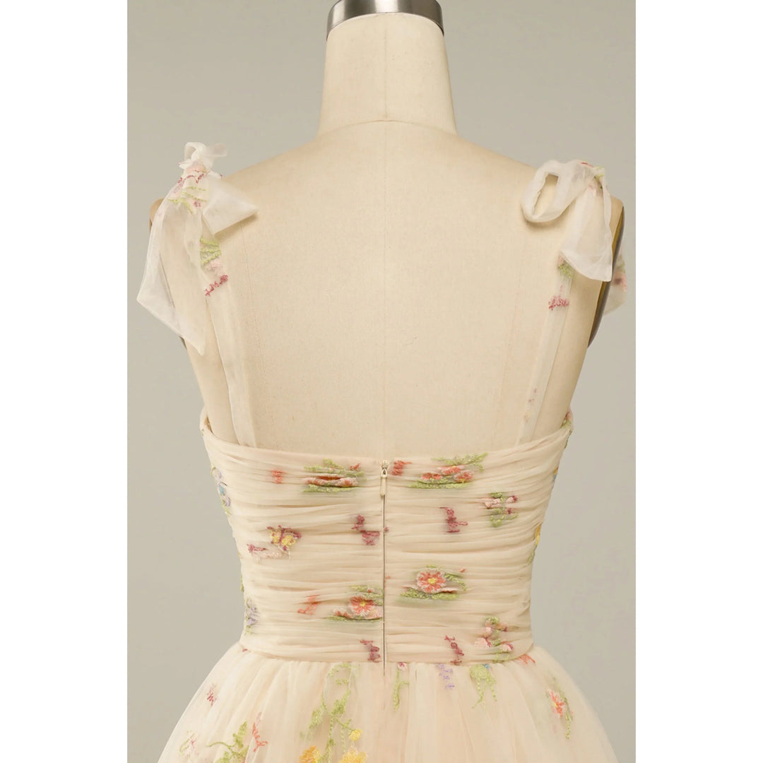 Beige nude : bustier plissé en tulle brodé de fleurs, bretelles en voile nouées et fermeture zippée au dos.