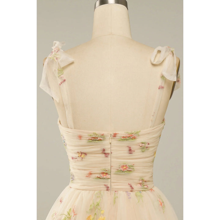 Beige nude : bustier plissé en tulle brodé de fleurs, bretelles en voile nouées et fermeture zippée au dos.