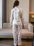 Vue de dos d’une femme portant un pyjama long en satin beige clair, décoré de motifs papillons noirs et feuillages fins. Ensemble composé d’un haut à manches longues avec col passepoilé noir et d’un pantalon fluide assorti. Tenue élégante et confortable, idéale pour des nuits paisibles ou des moments de relaxation à la maison.