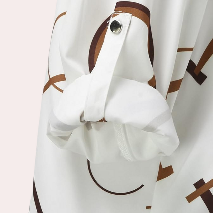 Détail du chemisier Opal pour femme, bouton de manche et tissu fluide blanc avec imprimé graphique marron, mettant en avant la finition soignée et le style élégant.