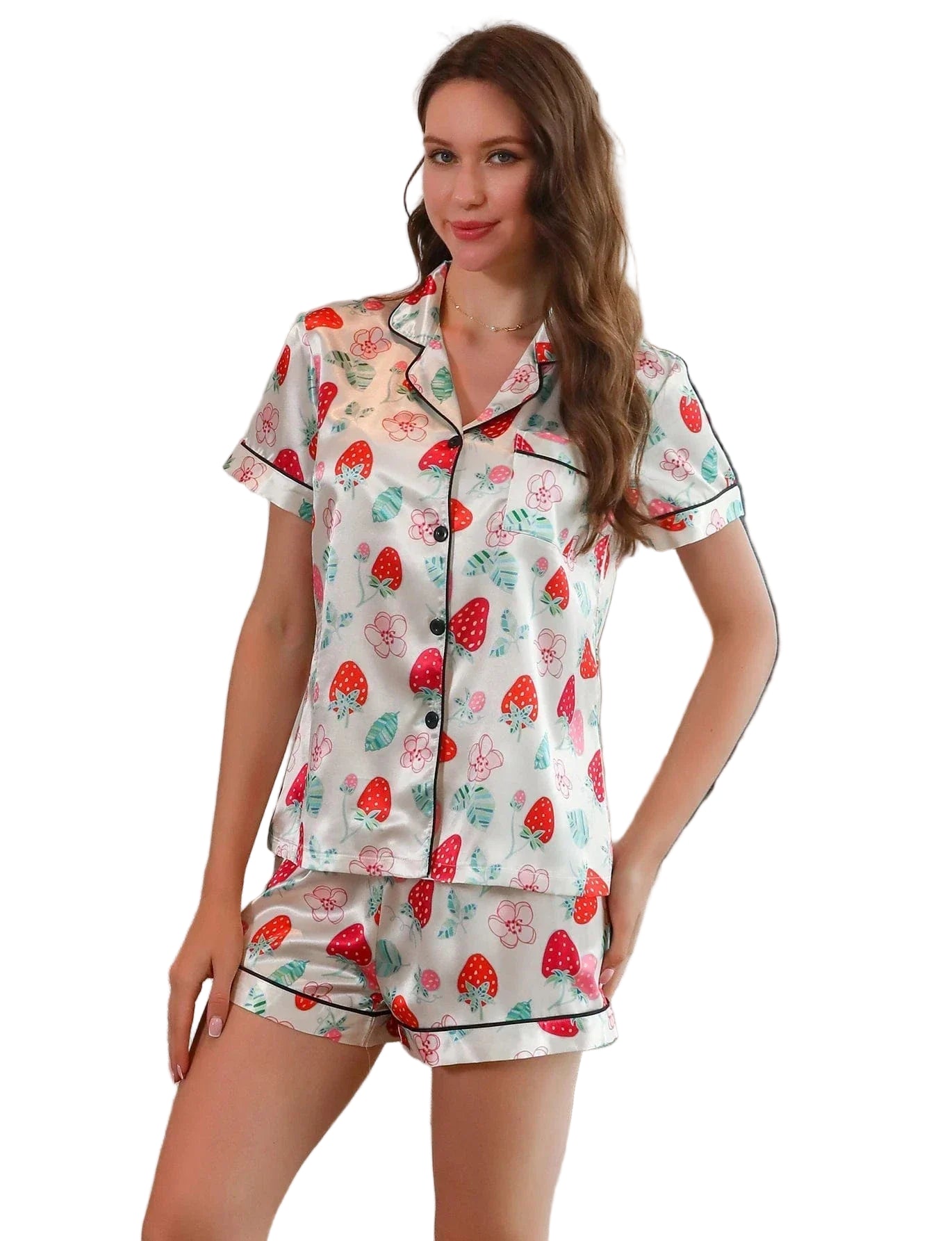 Femme portant le pyjama satin, un ensemble léger et élégant en satin blanc décoré de motifs de fraises rouges et de feuilles vertes, composé d’une chemise à manches courtes et d’un short assorti, photographiée dans un intérieur lumineux.