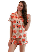 Femme portant le pyjama satin femme, un ensemble léger et élégant en satin beige, composé d’une chemise à manches courtes et d’un short assorti imprimés de grandes fleurs orange.