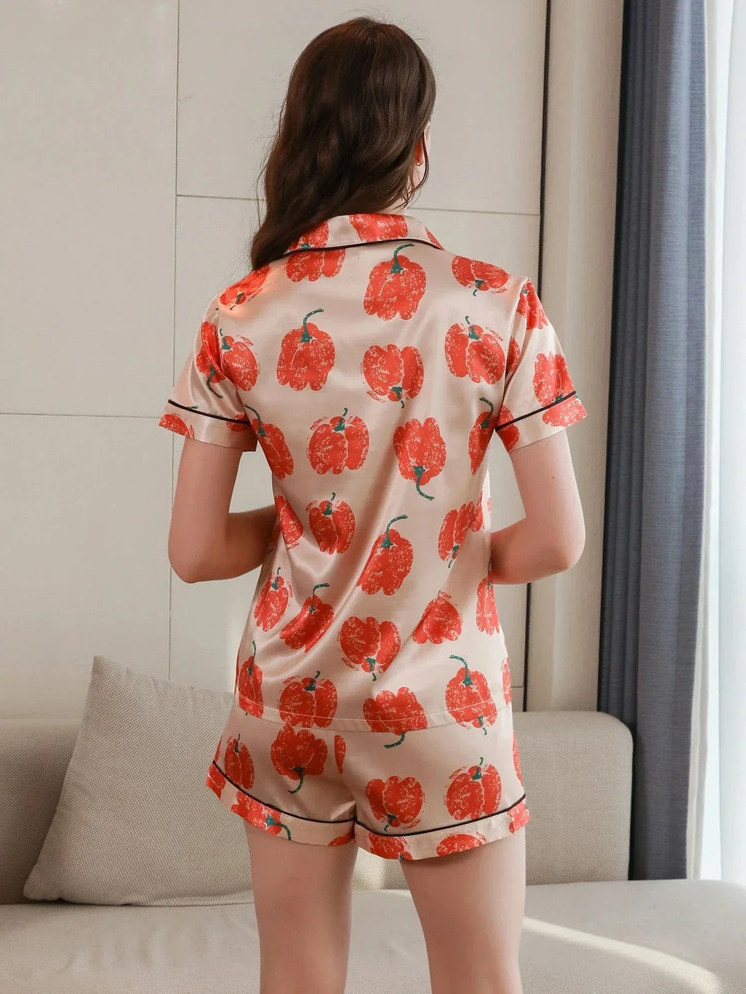 Femme vue de dos portant le pyjama satin femme, un ensemble léger et élégant en satin beige, composé d’une chemise à manches courtes et d’un short assorti, décorés d’un imprimé de grandes fleurs orange.