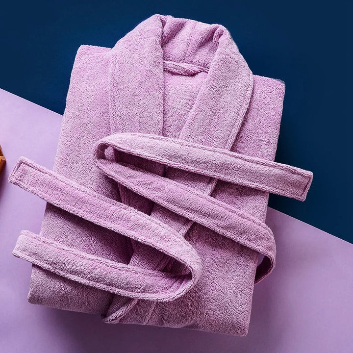 Peignoir Pascal pour homme, modèle épais et chaleureux en tissu éponge rose mauve, présenté plié avec sa ceinture assortie sur un fond coloré bleu et violet.