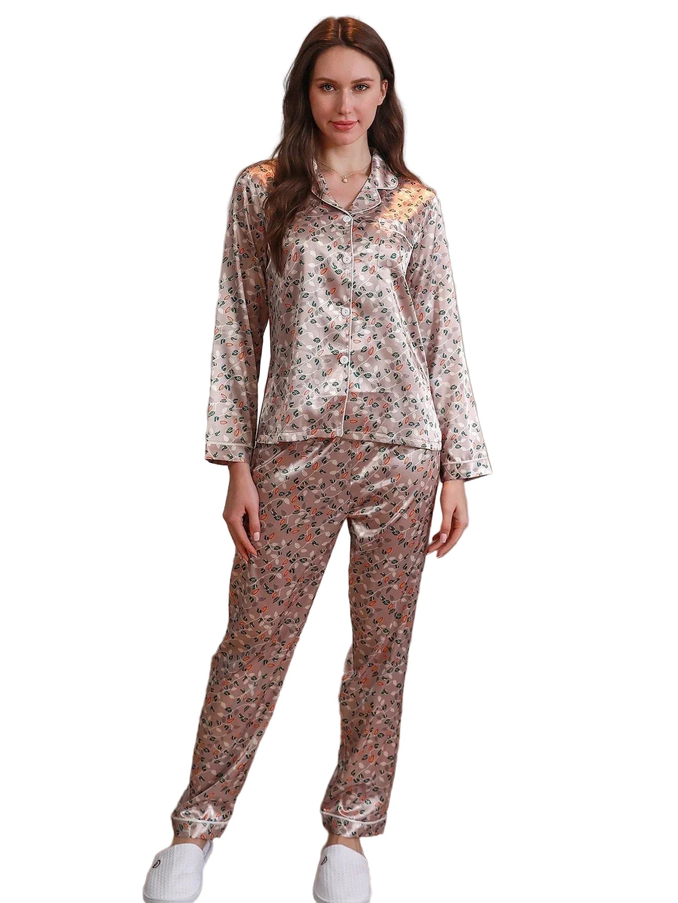Femme portant un pyjama long en satin rose clair imprimé de petits motifs floraux, composé d’un haut boutonné à manches longues avec col chemise et d’un pantalon assorti. Tenue tendance, douce et agréable, parfaite pour les nuits confortables ou les matinées cocooning.