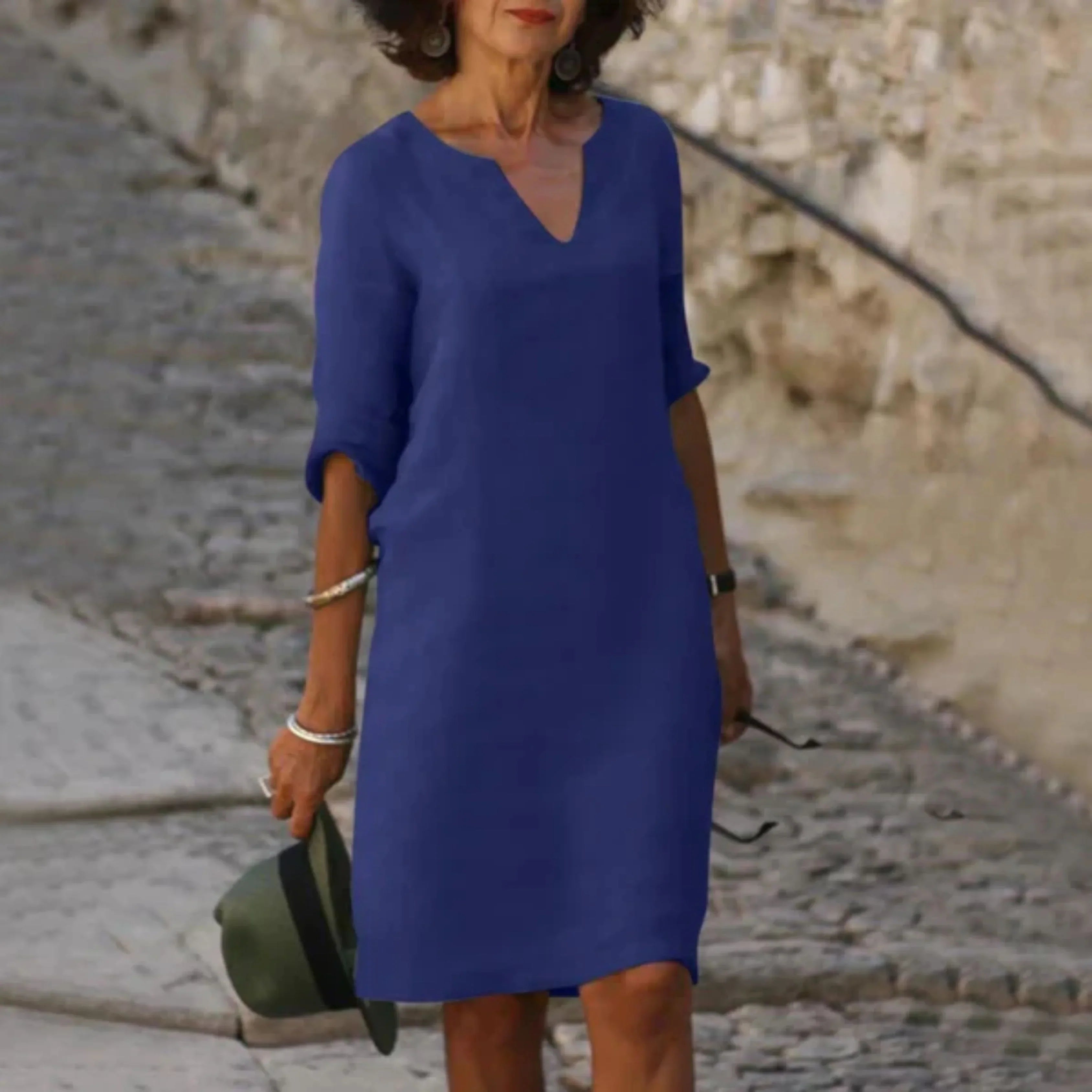 Bleu roi, coupe droite au-dessus du genou, col en V et manches 3/4 retroussées, en balade sur une rue pavée.