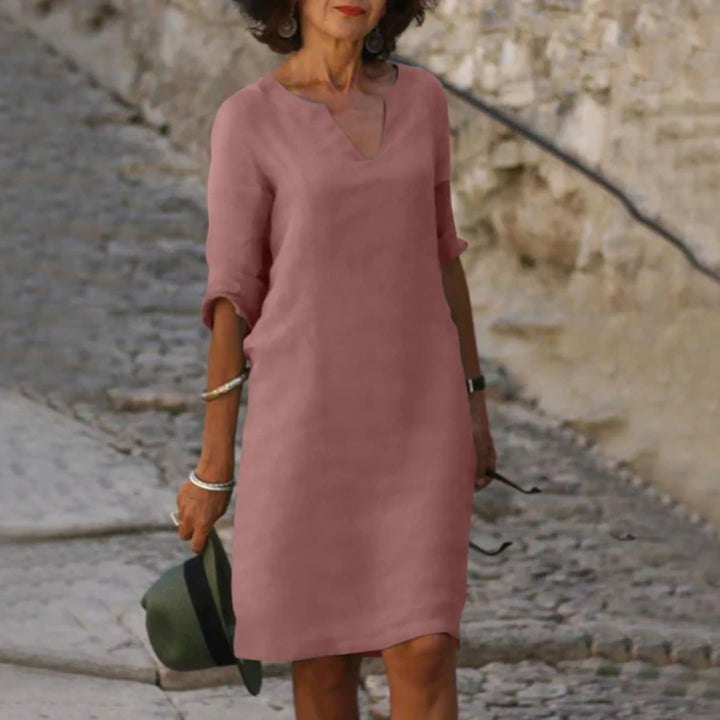 Rose poudré, coupe droite au-dessus du genou, col en V et manches 3/4 retroussées, en balade sur une rue pavée.