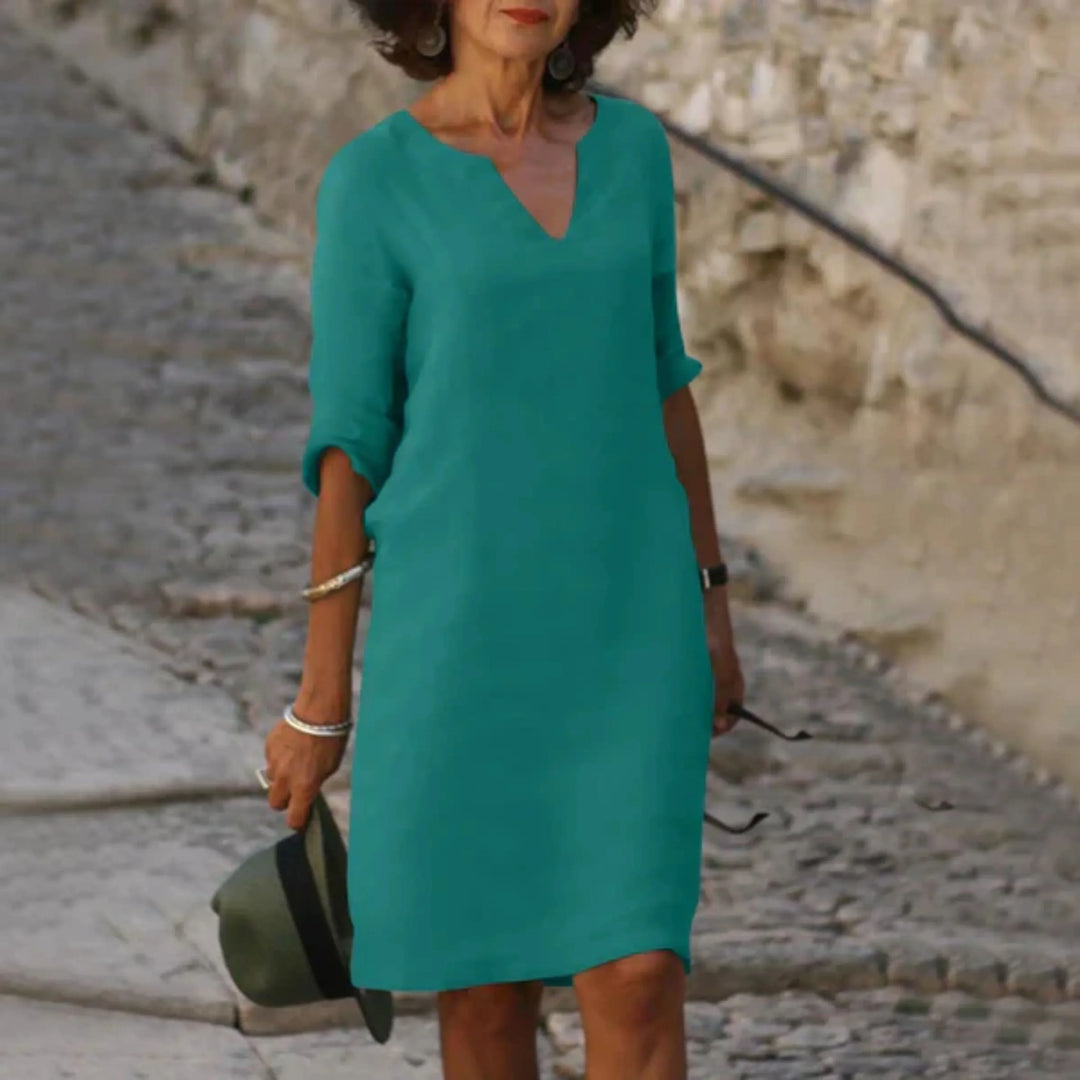 Vert turquoise, coupe droite au-dessus du genou, col en V et manches 3/4 retroussées, en balade sur une rue pavée.