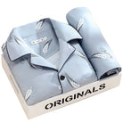 Pyjama premium pour homme présenté plié dans une boîte, en tissu bleu clair doux et respirant, avec motifs discrets de plume. Ensemble élégant et très confortable, idéal pour un sommeil agréable.