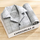 Pyjama premium pour homme présenté plié dans une boîte, en tissu gris clair à motif quadrillé fin avec bordures contrastées. Ensemble doux, respirant et très confortable, idéal pour des nuits paisibles et élégantes.