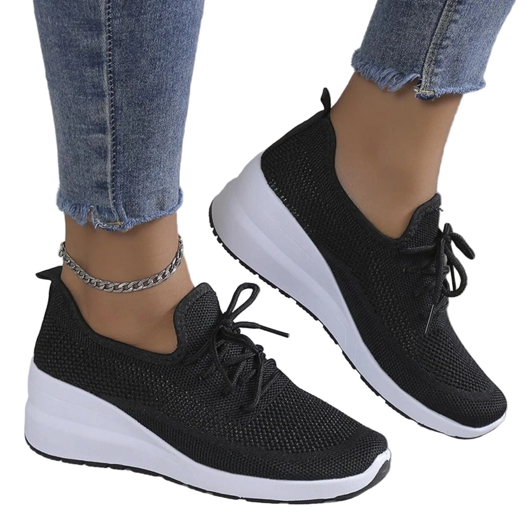 Baskets noires en maille respirante avec lacets et semelle compensée blanche, portées avec un jean, vue de profil.