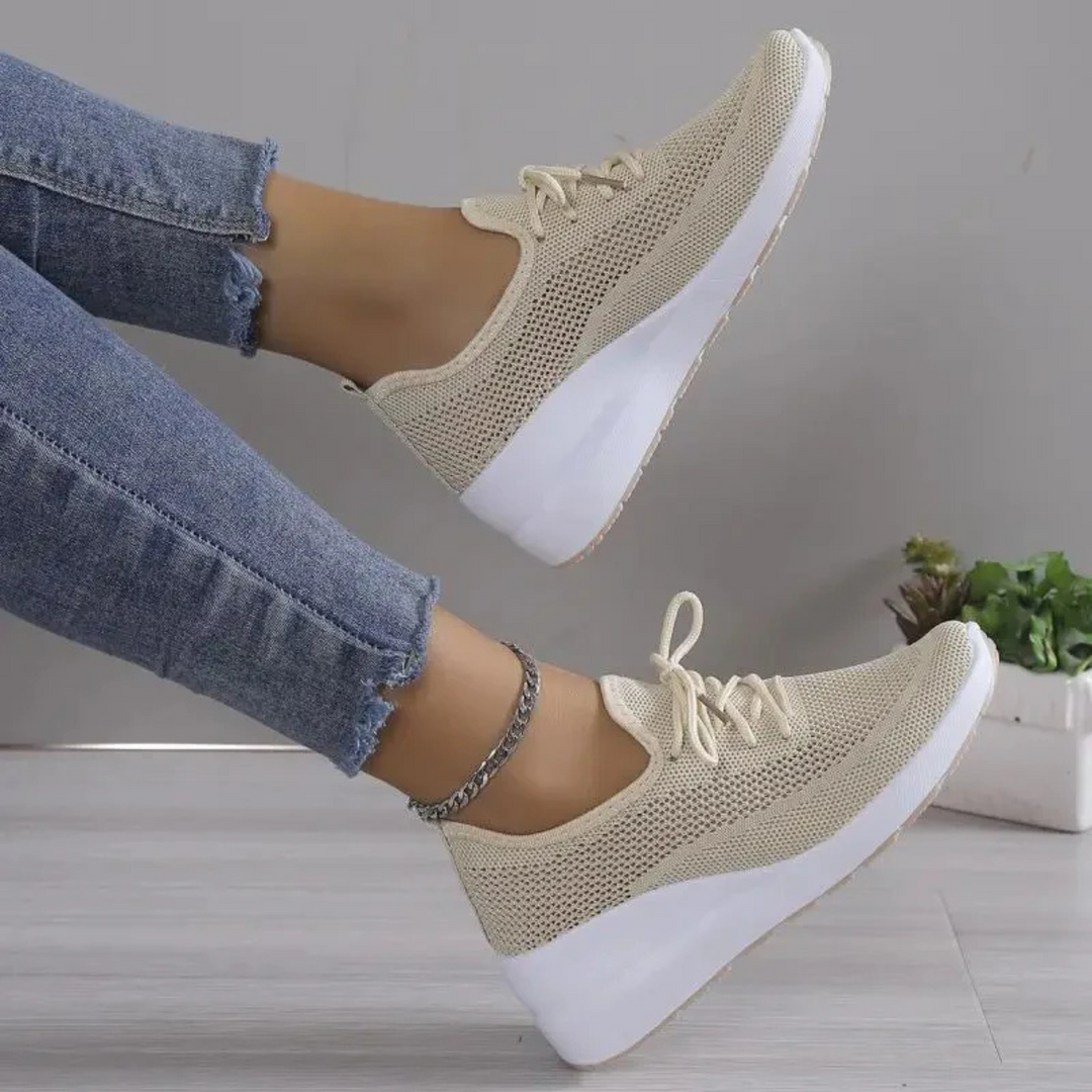 Baskets beiges en maille respirante avec lacets et semelle compensée blanche, portées avec un jean, vue de côté jambes levées.