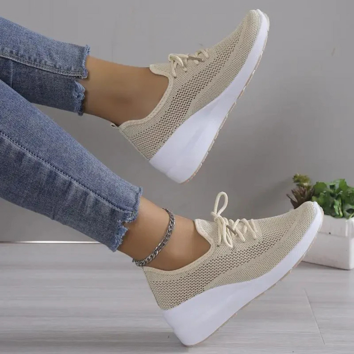 Baskets beiges en maille respirante avec lacets et semelle compensée blanche, portées avec un jean, vue de côté jambes levées.