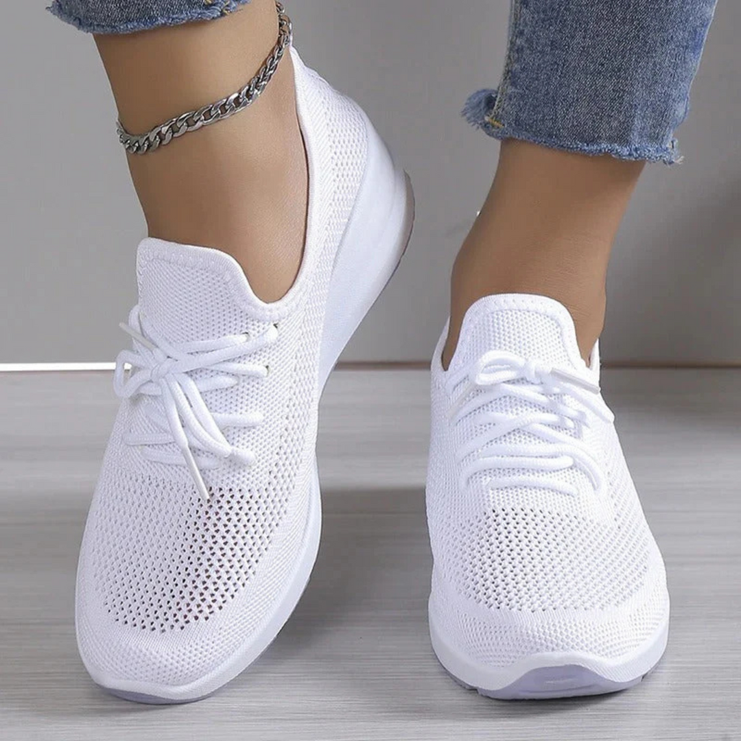 Baskets blanches en maille respirante avec lacets et semelle épaisse, portées avec un jean, vue de face en intérieur.
