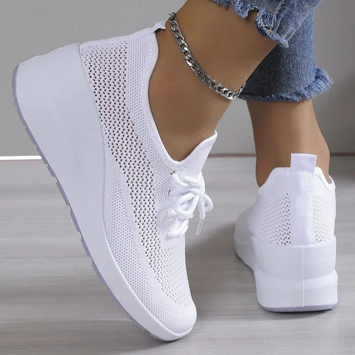 Baskets blanches en maille respirante avec lacets et semelle compensée, portées avec un jean, vue arrière et de côté.