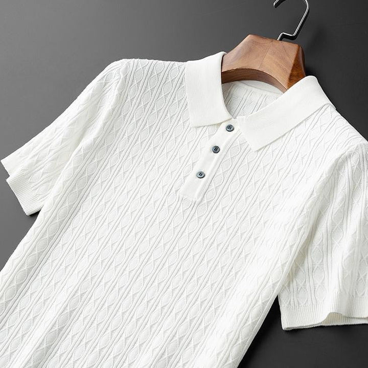 Polo blanc suspendu, avec un col raffiné et des boutons noirs contrastés, offrant un design moderne et une texture en maille élégante.