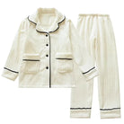 Pyjama femme deux pièces en tissu crème à texture côtelée, avec veste boutonnée à col châle, poches plaquées et finitions noires contrastantes. Ensemble chaud, élégant et très confortable, idéal pour l’hiver.