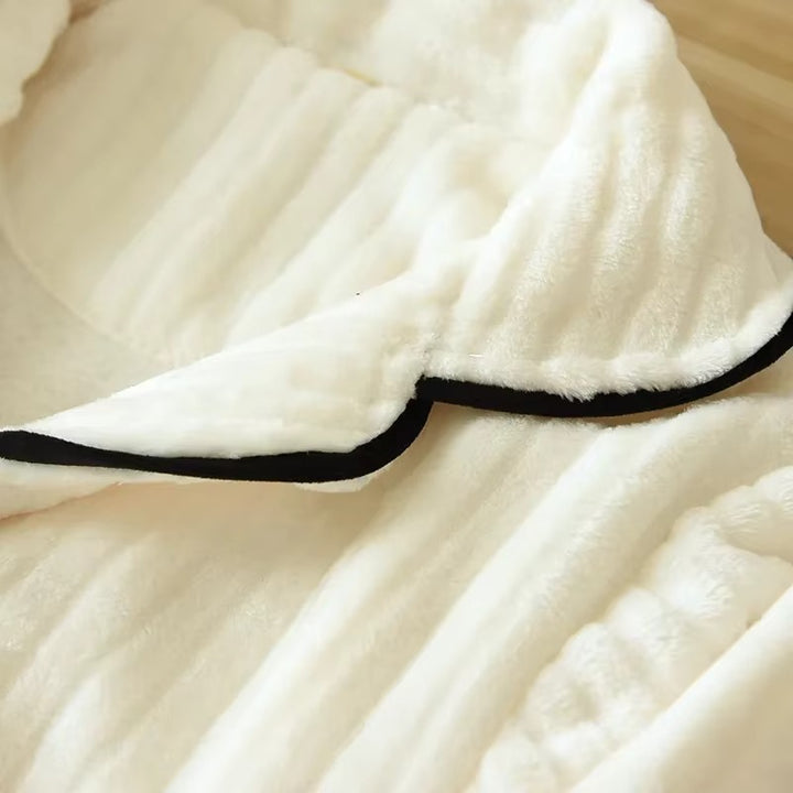 Gros plan sur le col en tissu doux et côtelé d’un pyjama femme crème, avec passepoil noir contrastant. Matière moelleuse et chaude, idéale pour les nuits d’hiver et le confort à la maison.