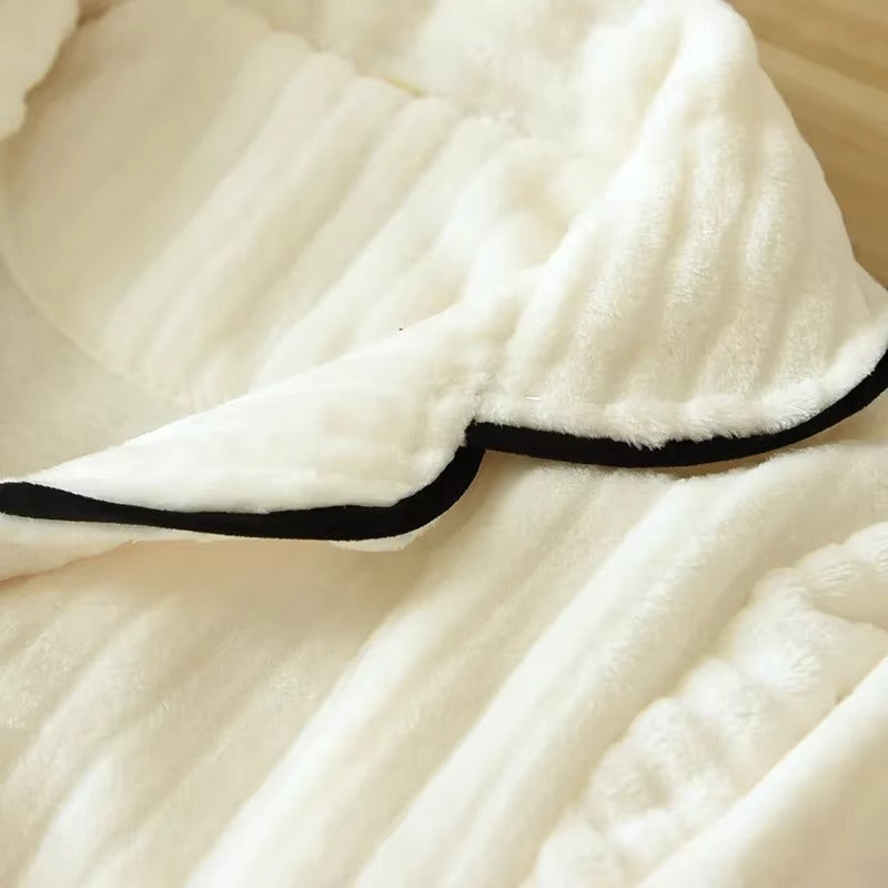 Gros plan sur le col en tissu doux et côtelé d’un pyjama femme crème, avec passepoil noir contrastant. Matière moelleuse et chaude, idéale pour les nuits d’hiver et le confort à la maison.